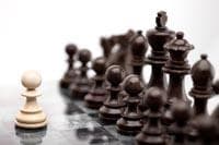 A single white pawn stands alone facing a large army of black chess pieces.