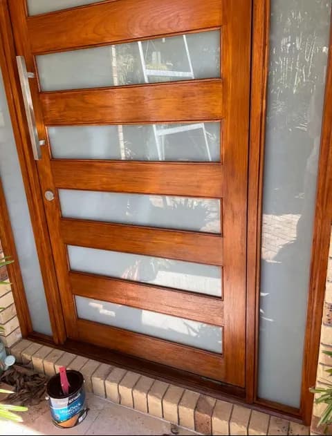 Freshly stained wooden door with five horizontal frosted glass panels and a long silver handle.