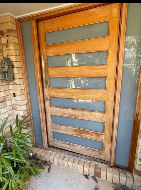 Light wood front door with five frosted glass panels and a long vertical silver handle.