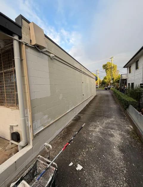 Beige brick wall being painted in a narrow alleyway with a paint roller in foreground.