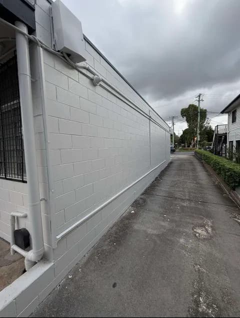 White cinder block wall bordering a narrow concrete driveway under a grey, overcast sky.